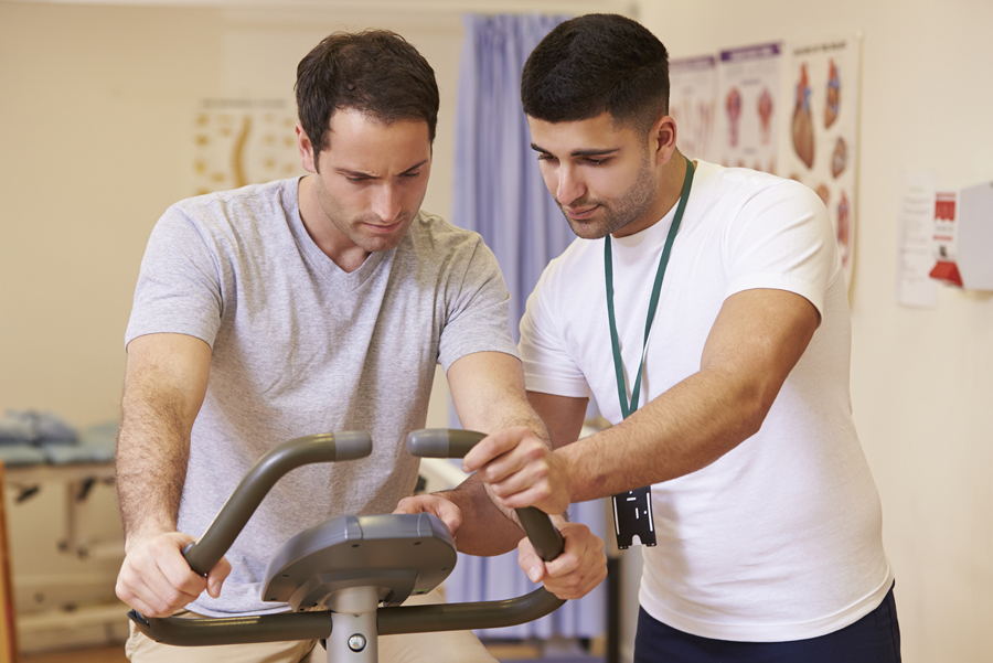 physical therapist assisting patient on excersise bike